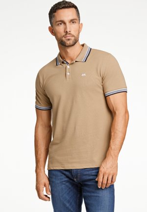 Polo shirt khaki con colletto classico, dotato di dettagli a strisce blu sul colletto e sulle maniche, abbinato a jeans in denim blu.