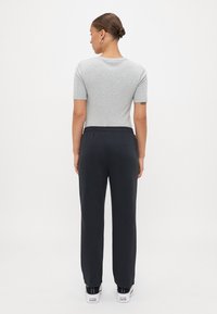 T-shirt grigio a maniche corte abbinato a pantaloni della tuta neri con vita elastica. I pantaloni hanno una vestibilità comoda e l'outfit è completato da sneakers bianche.