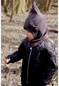 Chaqueta negra acolchada con cremallera plateada, combinada con una capucha ajustada de color púrpura oscuro con detalle de lazo. Niño sosteniendo un pequeño objeto al aire libre.