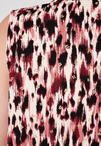 Tissu texturé avec un motif abstrait rouge, noir et blanc, agrémenté d'accents dorés, mettant en avant un mélange de formes et de taches irrégulières.