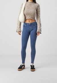 Suéter corto de manga larga en punto multicolor y jeans ajustados azules. La modelo lleva zapatillas negras con rayas blancas y un bolso blanco.