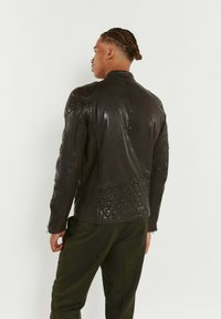 Veste en cuir noir avec épaulettes et panneau arrière matelassés, présentant un col montant et une fermeture éclair, vue de dos.