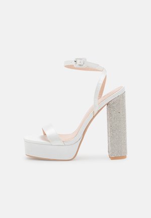 Sandale à plateforme blanche à talon haut avec bride à la cheville et boucle, dotée d'un talon bloc orné de petits strass.