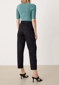 Teal ribbat tröja med korta ärmar, kombinerad med högmidjade svarta byxor. Svarta klacksandaler och en slät textur.