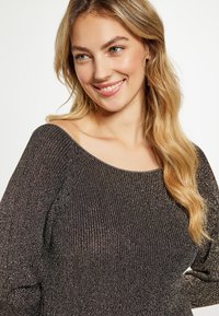 Fekete bordázott pulóver fémes részletekkel, váll nélküli nyakkivágással és hosszú ujjakkal. Puha tapintású, testhez simuló fazon.