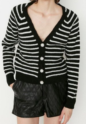 Zwart-wit gestreepte cardigan met een V-hals, voorzien van vijf decoratieve knopen. Draag het over zwarte, gewatteerde shorts.