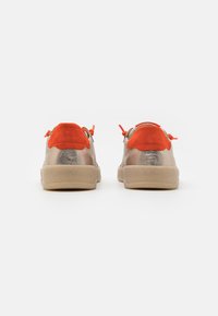 Beige Sneaker mit metallisch goldenen Seiten, orangen Wildlederakzenten an der Ferse und passenden Schnürsenkeln. Weicher Stoff mit runder Zehenpartie und flacher Sohle.