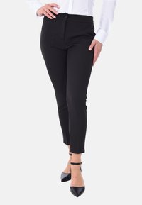 Pantaloni neri aderenti con una texture liscia, caratterizzati da una chiusura con bottone, lunghezza alla caviglia e spacchi sui fondi. Abbinati a tacchi neri.