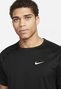 Camiseta atlética negra de manga corta con cuello redondo, que presenta un logo de Nike blanco en el lado izquierdo del pecho. Material suave y transpirable.