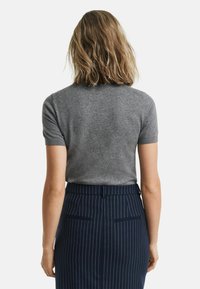 Maglione grigio a maniche corte realizzato in un materiale fine, abbinato a una gonna aderente a righe navy. Texture liscia e design su misura.