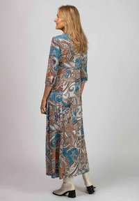 Lång, mönstrad klänning med paisleymönster i blått, brunt och krämfärgat. Trekvartslånga ärmar och en flödande siluett. Bärs med beige ankelstövlar.
