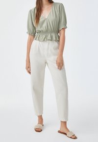 Blouse texturée vert clair avec un col en V et une taille marquée, associée à un pantalon écru taille haute et des sandales plates tressées.