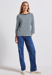 Gestreepte lange mouwen top in navy en wit, gecombineerd met hoge taille blauwe jeans. De textuur lijkt zacht; de broek heeft een losse pasvorm. Casual schoeisel inbegrepen.