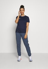 Marineblå atletisk t-shirt med korte ærmer og hvid kant, parret med grå sweatpants med sidelister og hvide sportssko.