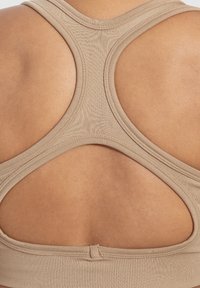 Beige urheilupaita, jossa on urheilullinen takaosa ja avoin leikkaus selässä, valmistettu sileästä ja venyvästä kankaasta.