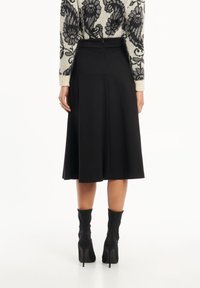 Zwarte plooienrok met een aansluitende taille en ritssluiting aan de achterkant, gekoppeld aan zwarte hooghals haklaarzen.