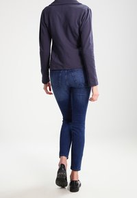 Námořnická přiléhavá bunda s límcem, v kombinaci s tmavě modrými slim jeansy a černými platformovými botami, pohled zezadu.