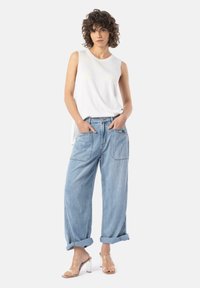 Lett hvit ermeløs topp med rund hals, sammen med lyseblå baggy jeans med store lommer og oppbrettede hem. Gjennomsiktige hæl sandaler.