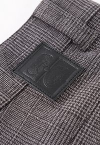 Gros plan sur un tissu gris à carreaux avec un patch rectangulaire en cuir noir cousu affichant un motif abstrait embossé.