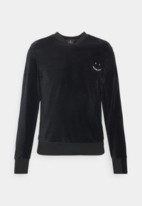 Sweat-shirt en velours noir avec manches longues, encolure ronde, et petit graphique de visage souriant blanc sur la poitrine. Poignets et ourlet côtelés.