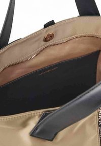 Beige lærred tote taske med sorte læderremme. Indvendigt har den en nudefarvet stofforing og en lynlås lomme. Guld prægede brandikoner er synlige.