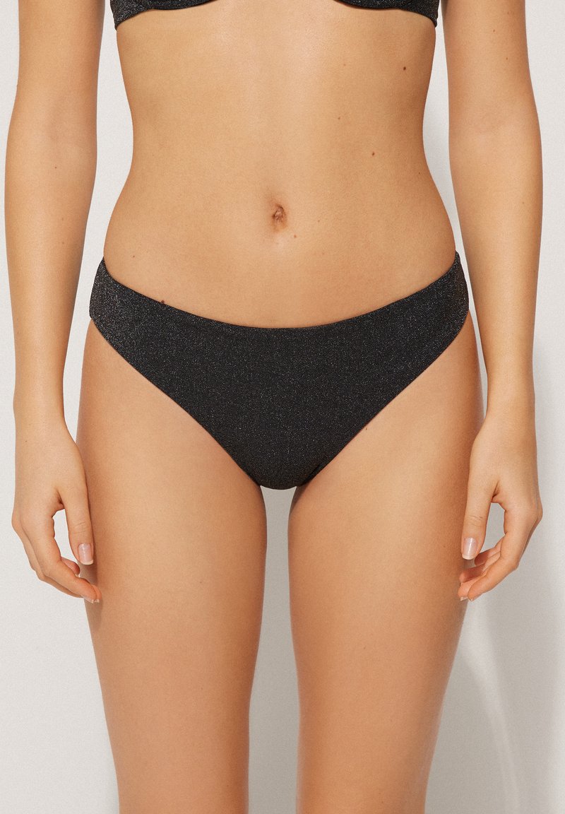 Černé bikiny s třpytivým, texturovaným materiálem. Nízký střih s širokým pasem a hladkými okraji.