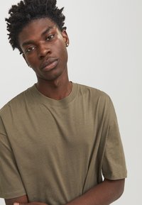 Olivenfarvet t-shirt med korte ærmer og rund hals, lavet af blødt stof, med en afslappet pasform og minimale syninger.