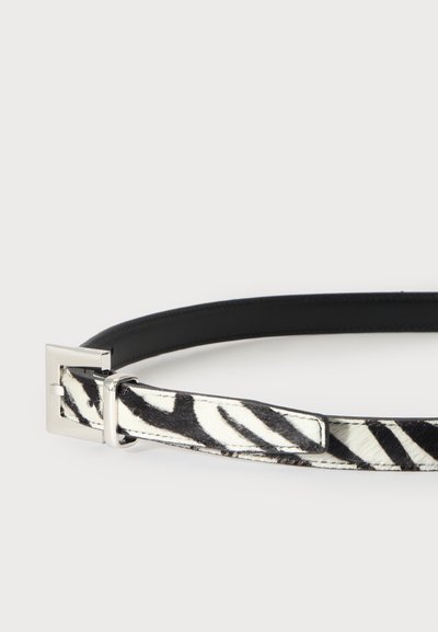 Ceinture fine imprimé zèbre noir et blanc avec une boucle carrée argentée sur fond blanc uni.