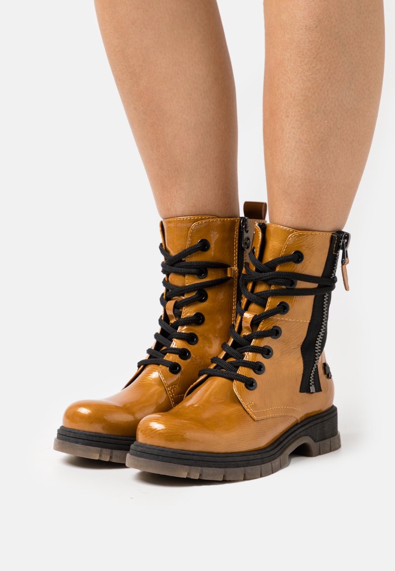 Bottines en cuir marron avec lacets noirs, fermeture éclair sur le côté et semelle robuste. Fini brillant et corps texturé. Présente une languette à l'arrière.