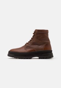 Bottines en cuir marron avec un dessus texturé, bout rond, col rembourré et semelle en caoutchouc noir avec un motif de semelle.