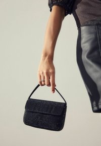Woman's hand holding a black studded handbag with a short handle, wearing a black leather skirt and a dark top.