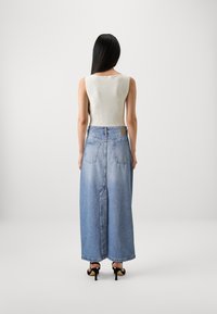 Débardeur blanc à côtes associé à une jupe maxi en denim bleu clair taille haute. La jupe présente deux poches arrière et une silhouette droite.