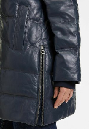 Marineblauer Ledermantel mit einem gesteppte Design, auffälligem Reißverschlussdetail an der Seite und glatter Textur. Verfügt über eine aufgesetzte Tasche am Oberarm.