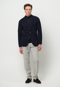 Blazer in misto lana blu navy con due tasche frontali, abbinato a pantaloni grigi chiari. Mocassini neri completano il look. Design semplice e sartoriale.