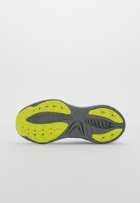 Semelle d'une chaussure de sport avec une base grise et des motifs de traction jaune vif, conçue pour l'adhérence et la flexibilité.