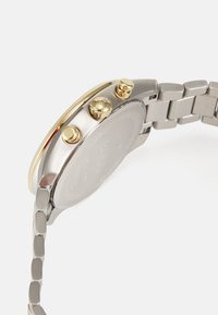 Edelstahlarmbanduhr mit silbernem Armband, goldenen Akzenten, drei Druckknöpfen und einem strukturierten Gehäuseboden.