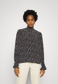 Blusa preta floral com gola alta, mangas longas e punhos franzidos. Apresenta padrões florais multicoloridos em tecido suave.