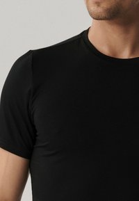 Czarna koszulka z krótkim rękawem wykonana z miękkiego materiału. Ma okrągły dekolt i dopasowany krój z minimalną ilością szwów oraz bez widocznych logo.