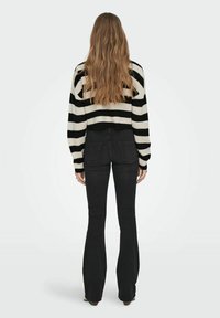 Maglione a righe bianco e nero in maglia con maniche lunghe abbinato a jeans neri a vita alta svasati. La texture sembra morbida e accogliente.