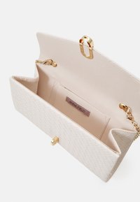 Beige woven handbag with gold hardware, clasp closure, and a chain strap. Features a smooth inner lining and a label stating "ANNA FIELD."