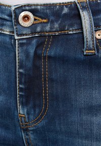 Dunkelblaue Denim-Jeans mit einer verblassten Textur, ausgestattet mit goldenen Nähten und einem silbernen Knopf mit eingeprägtem Markennamen.
