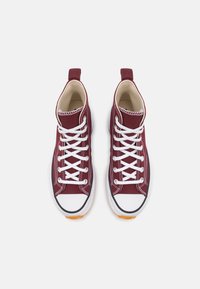 Vysoké tenisky z burgundské plátna s bílými tkaničkami, gumovým okrajem, kontrastním prošíváním a oranžovou gumovou podrážkou.