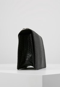 Borsa nera con motivo a coccodrillo strutturato, forma rettangolare, parti metalliche e apertura superiore. La superficie appare liscia con dettagli accurati.