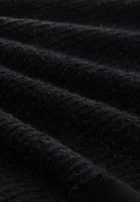 Schwarzer Stoff mit einem strukturierten, gerippten Muster. Weiche, flauschige Oberfläche mit sichtbaren Fasern, die Tiefe und Reichtum in Farbe und Textur zeigen.