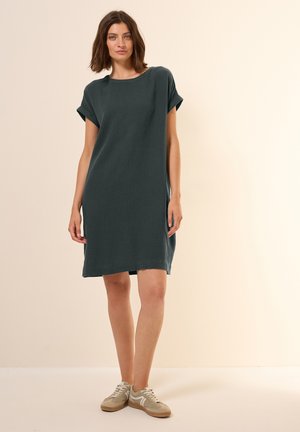 Dunkelgrünes Kurzarmkleid aus strukturiertem Stoff, mit lockerer Passform und umgeschlagenen Ärmelabschlüssen, kombiniert mit hellen Sneakern.