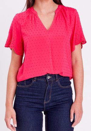 Femme portant un chemisier court rose vif avec des détails en dentelle ajourée et un jean bleu foncé taille haute.