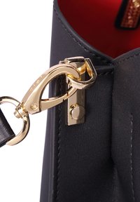 Binnenin zwarte leren tas met een goudkleurige sluiting en hardware. Heeft een gladde textuur, rode binnenvoering en een magnetische drukknoopsluiting.