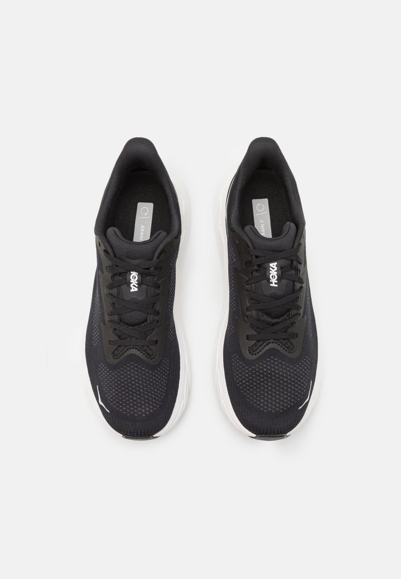 Czarne buty sportowe z siateczkową cholewką, okrągłym noskiem, białą podeszwą środkową i czarnymi sznurowadłami. Zawierają logo na języku oraz subtelne akcenty po bokach.