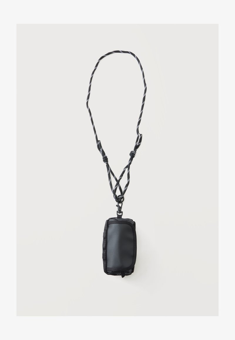 Pochette compacte noire avec fermeture éclair attachée à une sangle de cou réglable noire et blanche à motif sur fond blanc.
