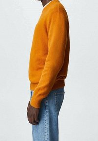 Pull orange à encolure ronde, en tissu doux, avec des poignets et un ourlet côtelés. Associé à un jean denim bleu clair.